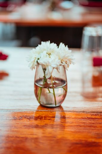 A vertical closeup shot of the white flowers in the glass vase on the wooden table in the restaurant
