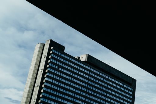 A low angle shot of a modern business building with big windows under a cloudy sky and sunlight