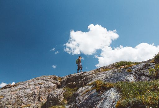 A low angle shot of a male with a backpack standing on the edge of the mountain with a cloudy sky in the background