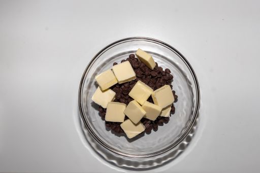 Many pieces of butter and tiny dark chocolate  in a transparent bowl on a white table