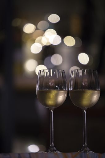 A vertical selective focus shot of two glasses of drink with the blurry lights in the background
