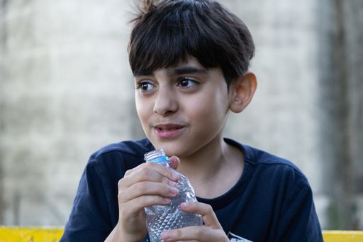 A closeup of a young Caucasian boy drinking a bottle of water  outdoors