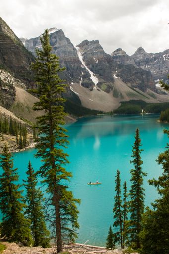 A vertical shot of people canoeing in the water surrounded by mountains under a cloudy sky