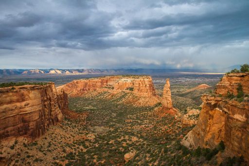 An aerial shot of a desert with cliffs and trees under a cloudy sky