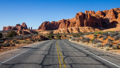 A beautiful shot of an empty road in the middle of a desert with bushes and cliffs in the distance under a blue sky