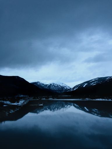 A vertical shot of water with snowy mountains in the distance under a cloudy sky