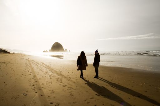 A couple walking on a beach shore with a bright sky in the background