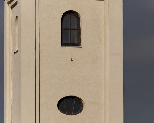 Picture of an exterior detail of a church with a glass arch window against a blue sky