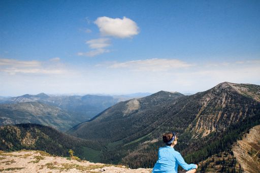 A female sitting on the mountain enjoying the view of trees and blue sky at daytime