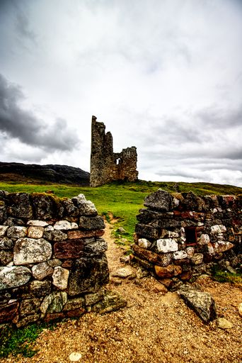 A vertical shot of stone castle ruins in wilderness under the gloomy sky with grass on the ground
