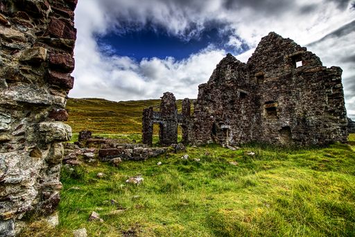 Old stone castle ruins in wilderness under the bright sky with a stone wall on the foreground