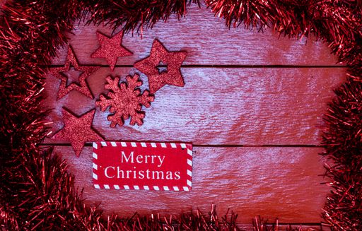 A Christmas garland around a red wooden board with decorations and copy space in the middle