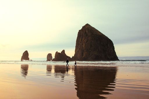 A beautiful shot of a kid running towards the water near its father with a rock and beautiful sky in the background