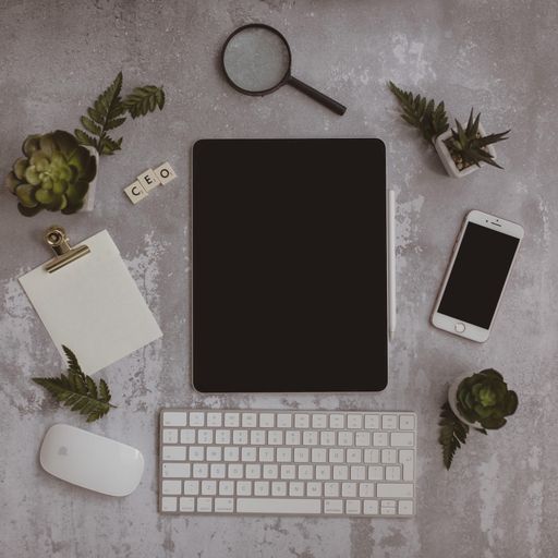 A keyboard, tablet with a black screen, smartphone, plants, magnifier and "CEO" made of scrabble blocks