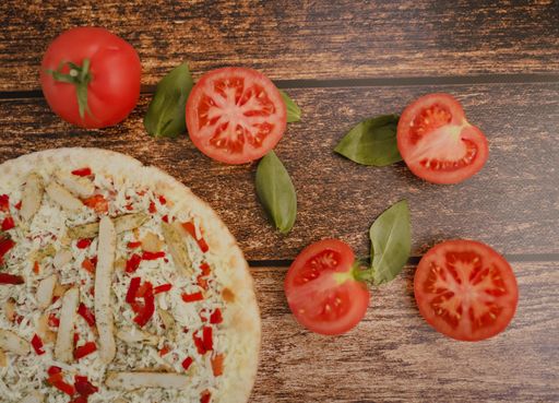 A high angle shot of sliced tomatoes and chicken pizza on a wooden surface