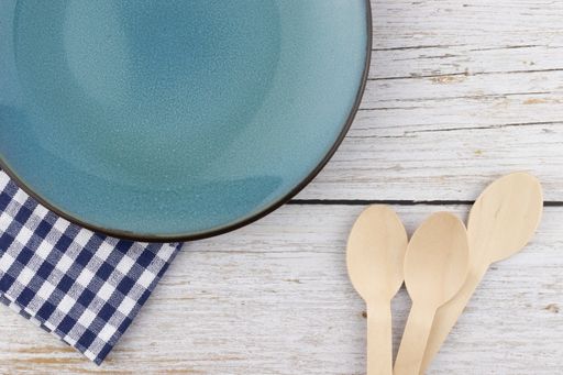 The wooden disposable spoons with a blue plate and a checkered napkin on wooden background