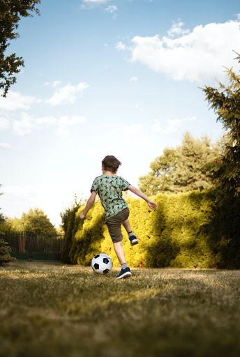 A vertical shot of a little boy kicking the soccer ball in the field