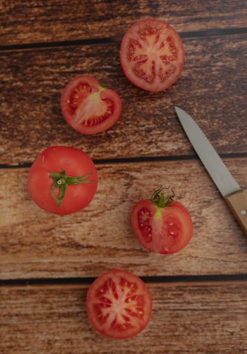 A vertical high angle shot of a knife and cut tomatoes on a wooden surface
