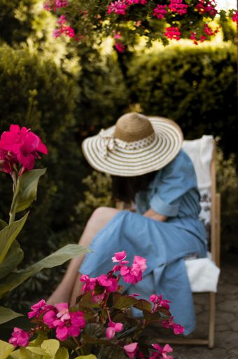 A vertical shot of a female in a straw hat behind the pink flower bush