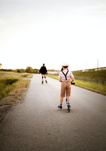 A vertical shot of a boy riding a scooter and a roller skater in the background