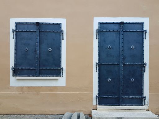 A view of the metallic shutters for door and window with forged details in a wall of a beige building