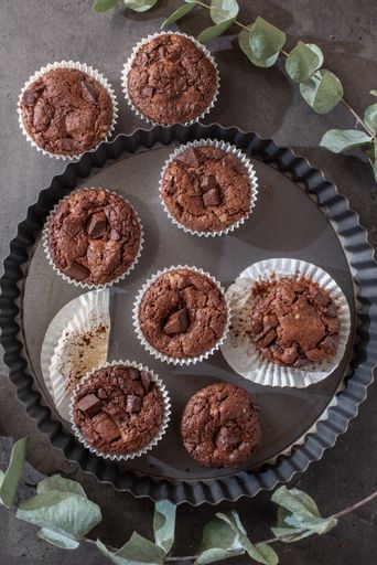 A vertical shot of sweet dark cupcakes on a tray with eucalyptus leaves on a table