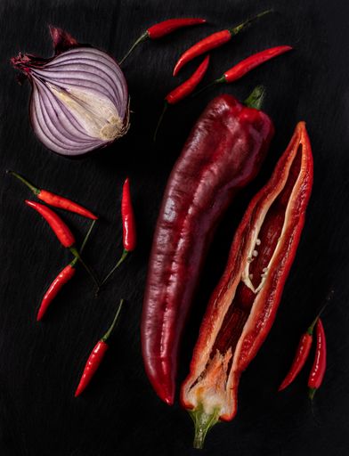 A vertical high angle shot of big and small red peppers and onion on a black surface