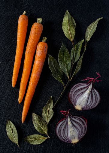 A vertical high angle shot of carrots, onions, and green leaves on a black surface