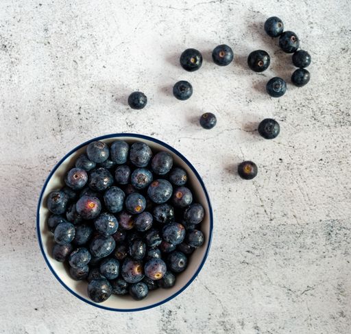 A high angle shot of a bowl full of blueberries with some blueberries scattered on a white surface
