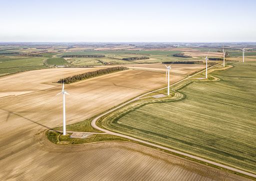 An aerial shot of the turbines on the beautiful green fields near the plowed farms