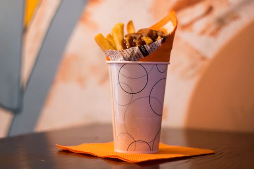 The French fries with a sauce on top in a cup on a yellow napkin on a wooden table