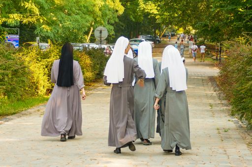 A group of nuns walking on a footpath at a park.