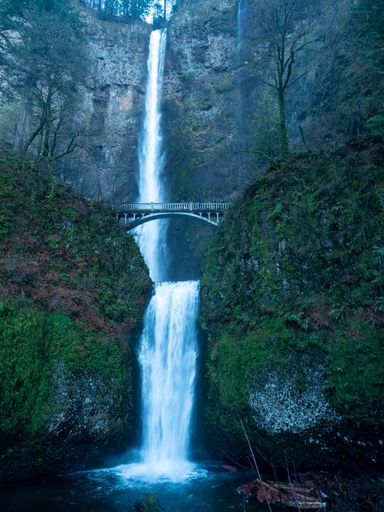 A vertical shot of a beautiful long waterfall under a bridge
