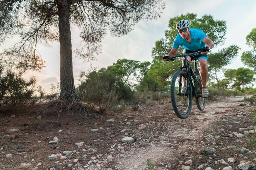 A fit male in a blue shirt riding a bike on a dirt trail