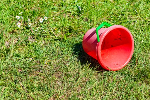 A closeup shot of a red bucket on the ground covered in the grass under the sunlight