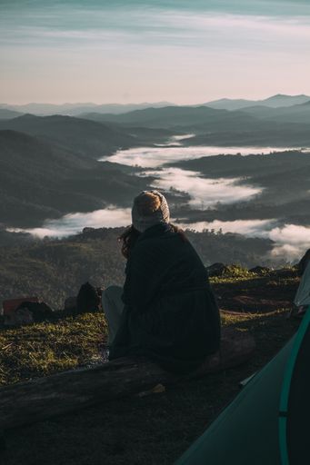 The behind shot of a young girl sitting on the log enjoying the landscape view of the mountains