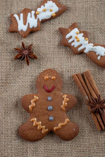 A vertical shot of a gingerbread cookie with cinnamon sticks next to it on a burlap cloth