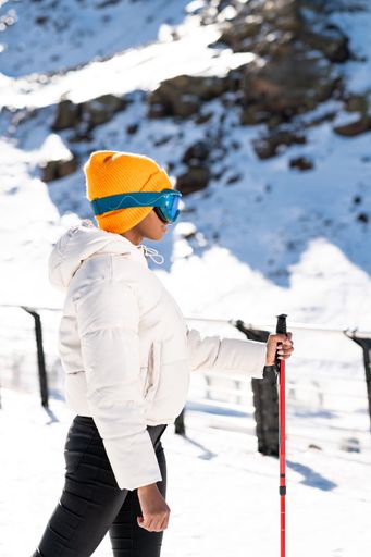 A vertical closeup of the young African American skier in snow goggles and a white down jacket.