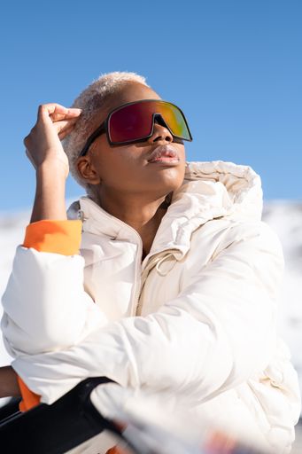 A vertical closeup of the young African American woman in snow goggles and a white down jacket.