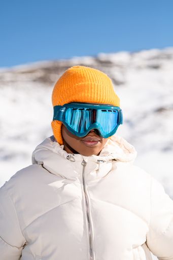 A vertical closeup of the young African American woman in snow goggles and a white down jacket.