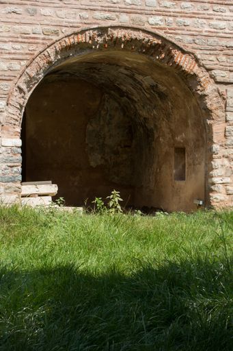 A vertical shot of a stone arch on a grass field foreground