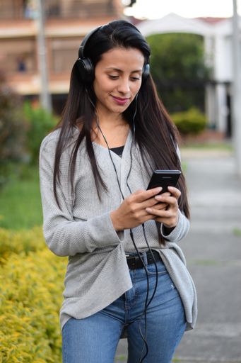 A vertical shot of a Hispanic woman listening to a song from her phone with headphones.