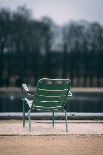 A vertical shot of a green chair near the lake in the park