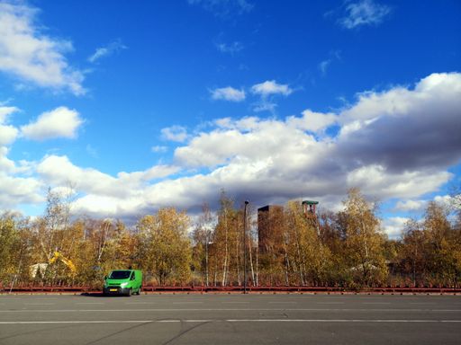 A green van in an empty parking lot with blue sky and clouds