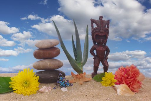 A closeup of Tiki Statue on Sand With Flowers and Sea Shells. Beach Scenery