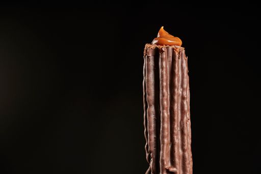 A close up shot of a churro filled with dulce de leche dipped in chocolate isolated on black background