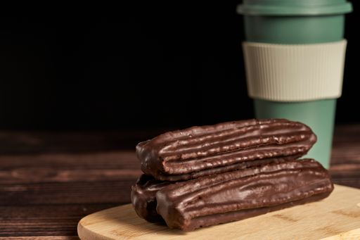 A close up shot of churros dipped in chocolate on a wooden board and a cup of coffee in the background