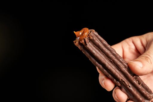 A close up shot of a hand offering churro filled with dulce de leche dipped in chocolate