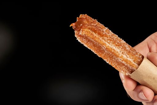 A close up shot of a hand holding churro filled with dulce de leche on black background