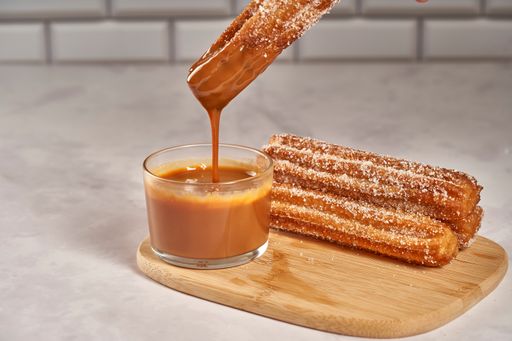 A close up shot of dipping churro in dulce de leche caramel and a wooden board with churros